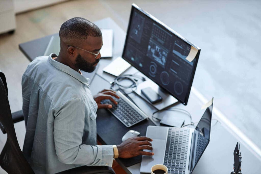 A man with glasses working on a laptop with a second monitor